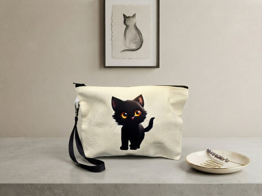 Kleine beige Stofftasche mit niedlicher schwarzer Katze DTF-Druck, Reißverschluss und Handschlaufe – Lifestyle-Setting mit Katzen-Kunstdruck im Hintergrund, von fks-design
