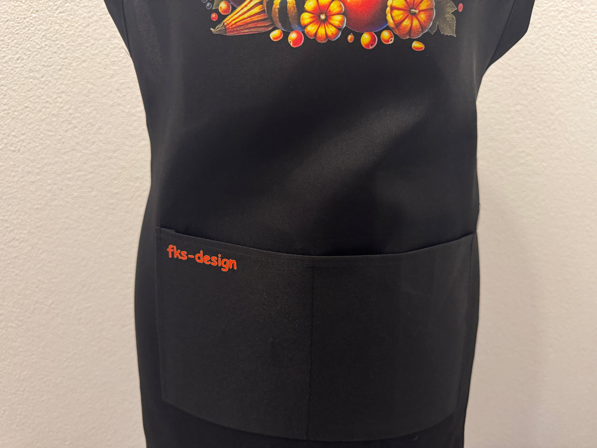 Detailansicht schwarze Kochschürze "Herbst Vibes" mit Kürbis-DTF-Druck und fks-design Schriftzug auf der Tasche – von fks-design
